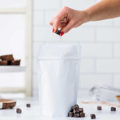 Hand dropping a baked brownie piece into a white pouch