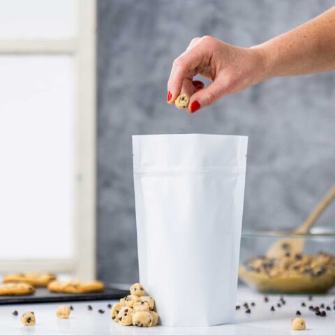 hand dropping a piece of chocolate chip cookie dough into a white pouch